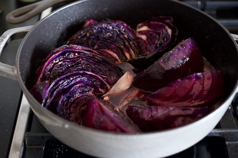 seared cabbage wedges arranged in pot with broth to halfway up.