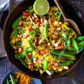 Indian fried rice with chilies and peanuts and lime half in cast iron skillet with wood utensil, a popular Indian recipe.