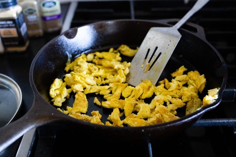scrambled eggs chopped with metal spatula in cast iron skillet.