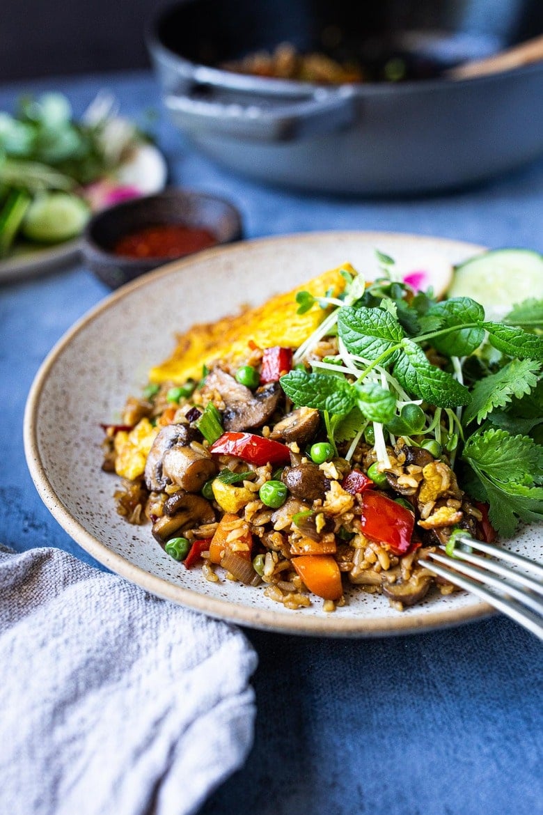 plate of Nasi Goreng (Indonesian Fried Rice) with peas, peppers, carrots, mushrooms, with fresh herbs.