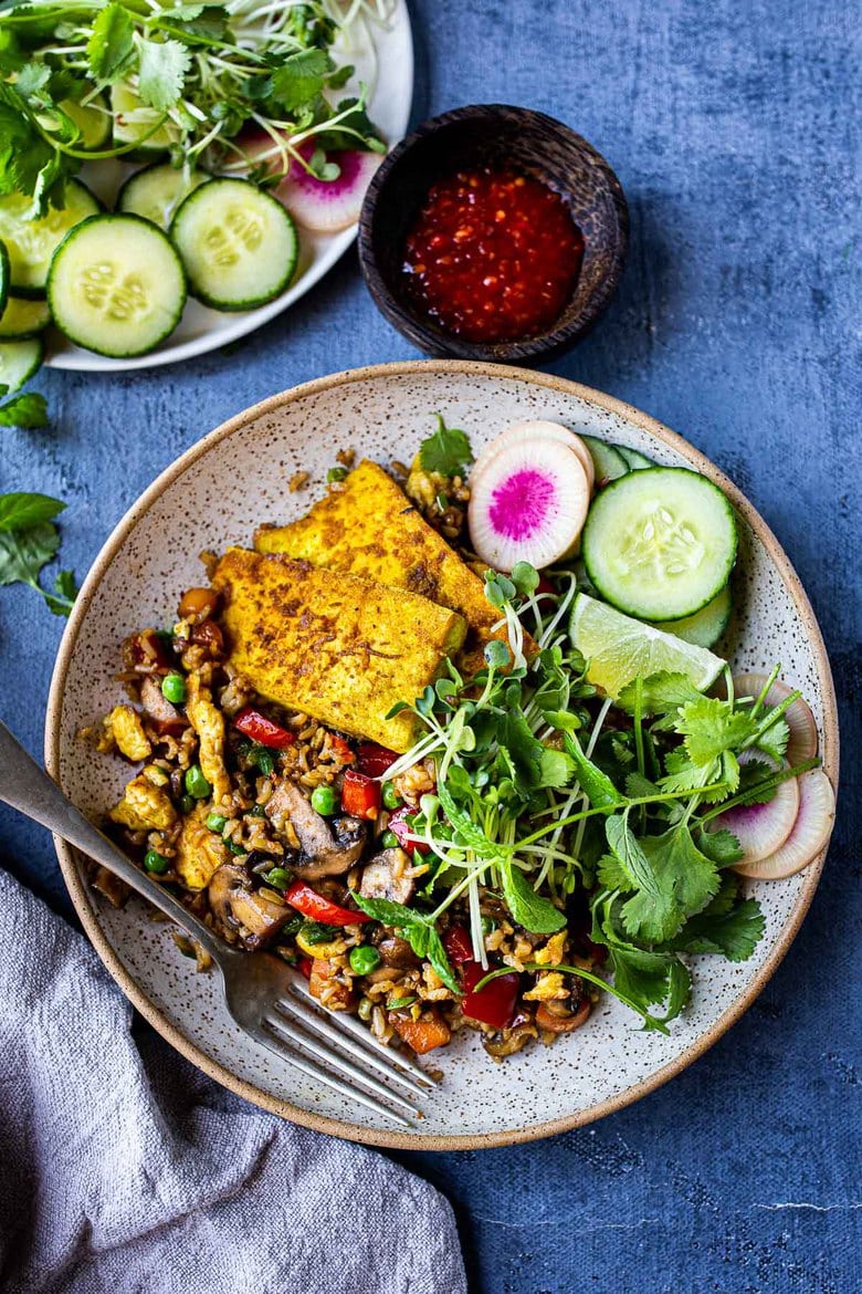 plate with nasi goreng (indonesian fried rice) with turmeric tofu and sprouts, herbs, cucumbers, radish, lime.