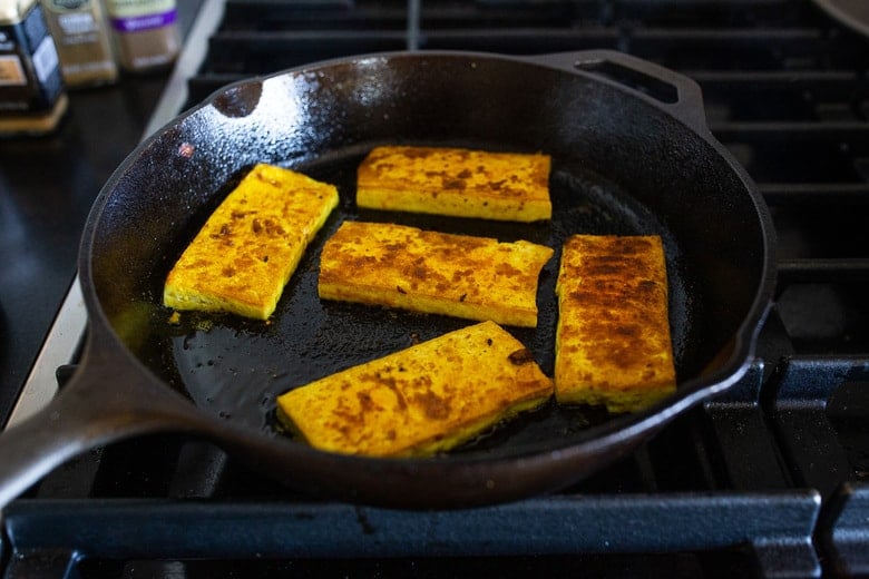 crispy turmeric tofu frying in cast iron skillet.