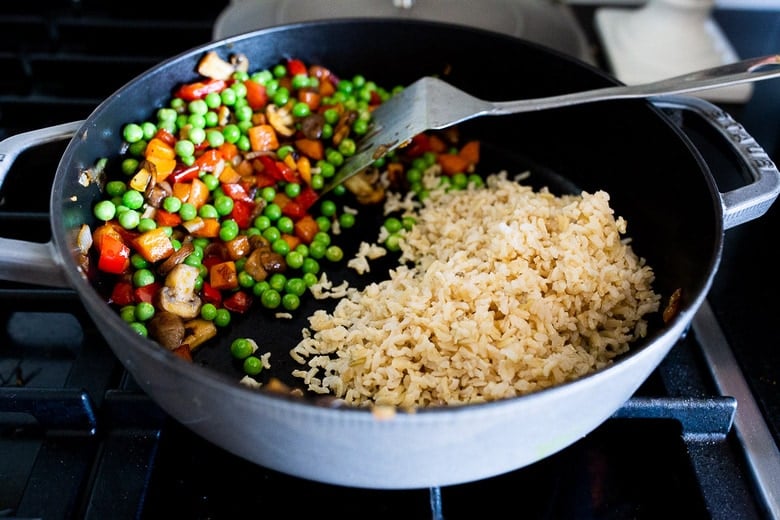 sautéed veggies on one side of pan with brown rice on other side, preparing to make fried rice.