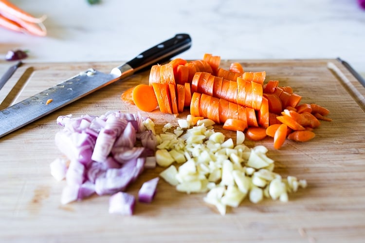 ingredients for carrot pasta chopped on wood cutting board with sharp knife- carrots, garlic, shallots.