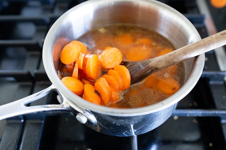 cooked sliced carrots in pot with water, tender and bright orange.