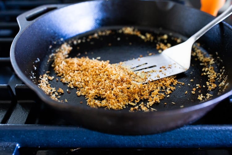 toasted breadcrumbs in cast iron skillet with metal spatula.