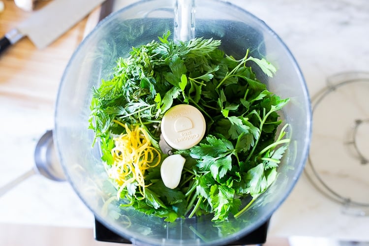 ingredients for carrot top gremolata in food processor- carrot tops, parsley, lemon zest, garlic.