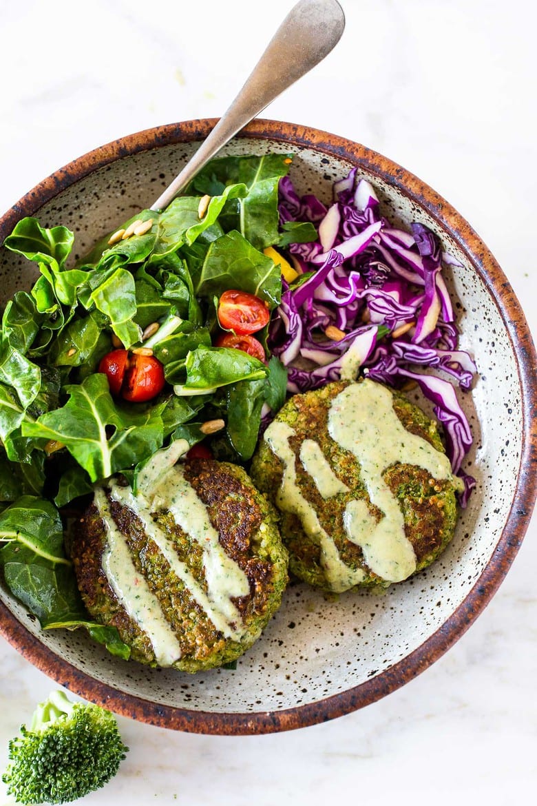 broccoli quinoa cakes with vegan cilantro crema drizzled over top, served in bowl with green salad and red cabbage.