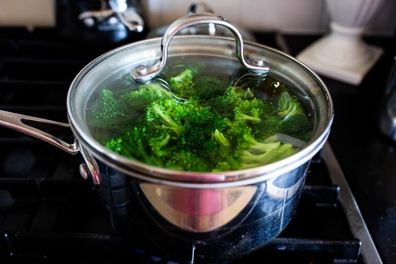 fresh broccoli florets in saucepan with lid over top steaming on stovetop.