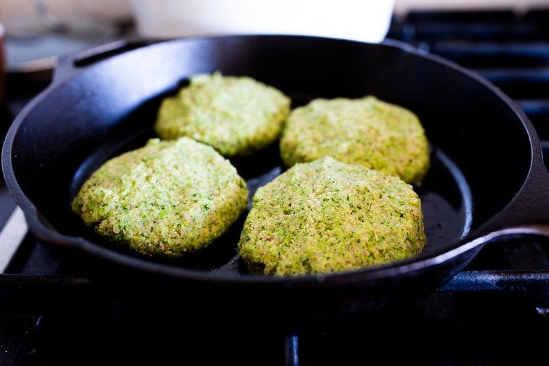 broccoli quinoa cakes formed into patties on cast iron skillet, frying.