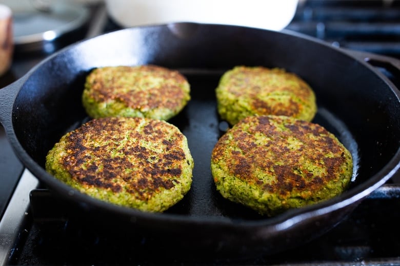 broccoli quinoa cakes frying on cast iron skillet with top side already seared.