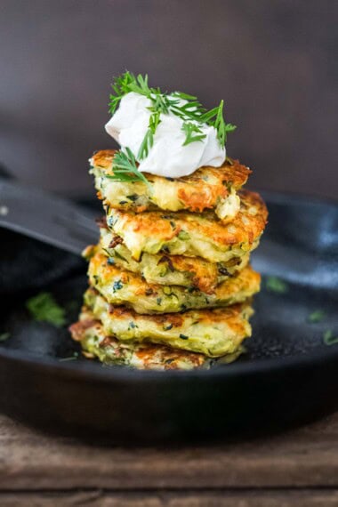 zucchini fritters stacked on plate topped with tzatziki sauce and fresh dill.