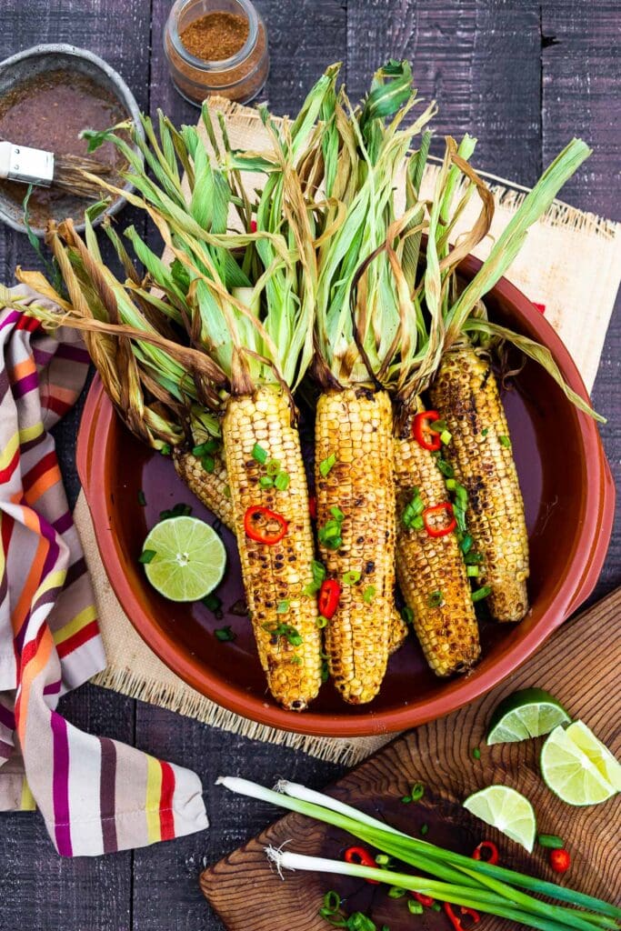 grilled corn on the cob with red chiles, sliced green onions, and a lime half.