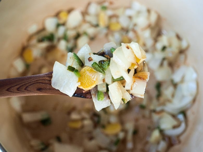 wood spoon holding up sauteed aromatics above soup pot.