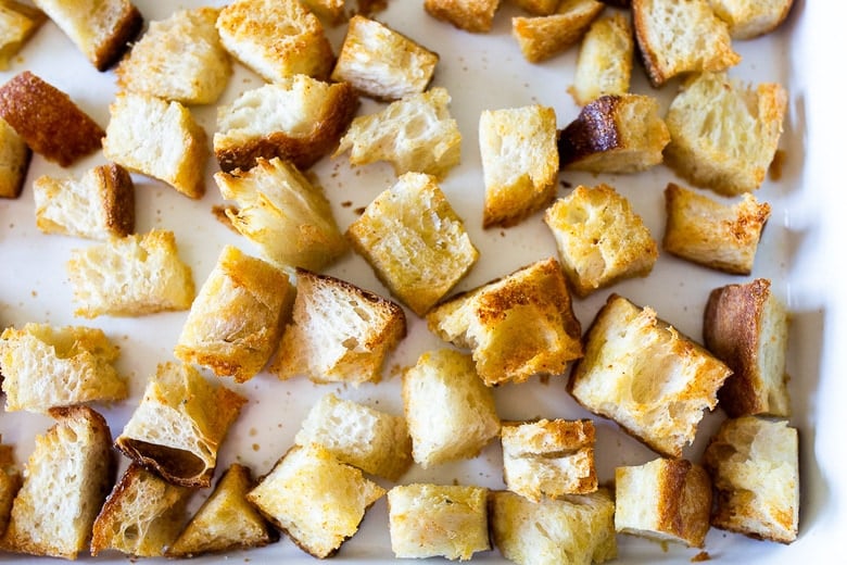 cubed and baked homemade sourdough croutons spread out evenly on baking sheet.