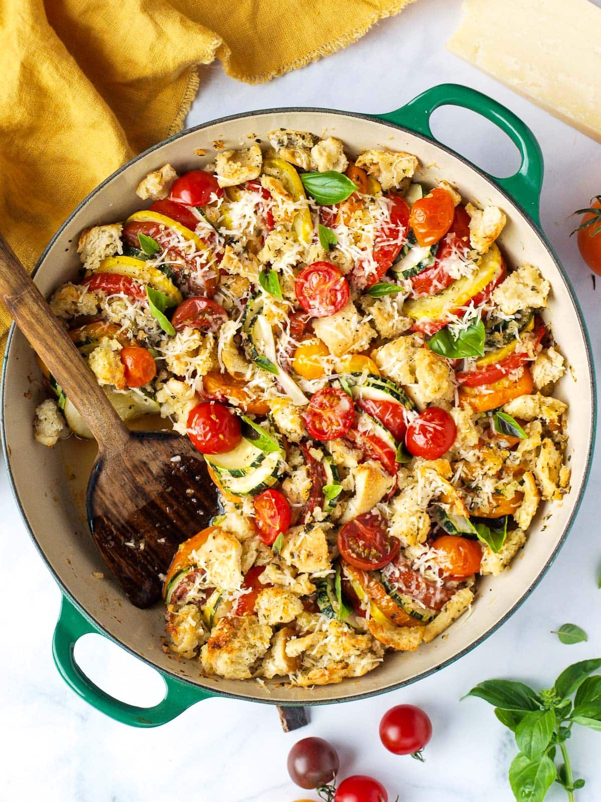 round baking dish with tomato zucchini gratin with wood serving spoon, blistered cherry tomatoes, and grated cheese. 