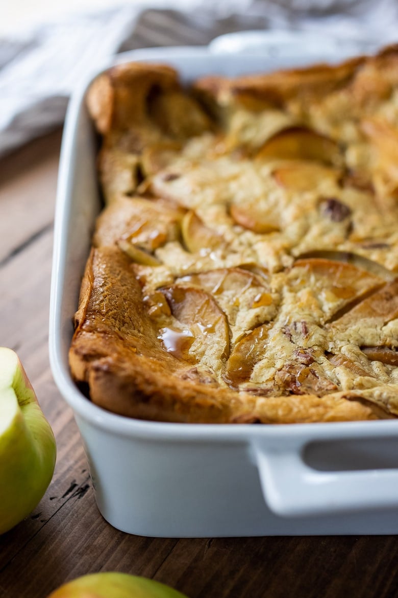 baked apple pannekoeken recipe in casserole dish with drizzle of maple syrup. 