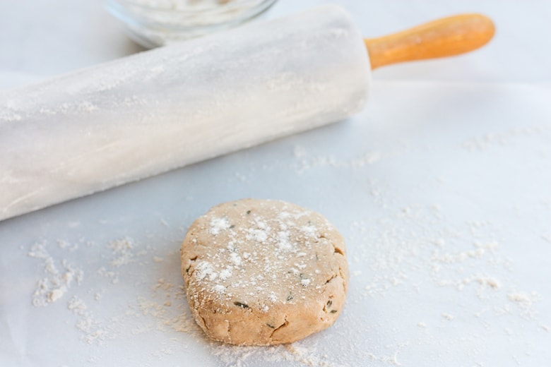 sourdough discard dough in round shape, with floured surface, next to rolling pin.