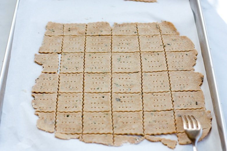 using a fork to prick the dough of the cut sourdough cracker pieces.