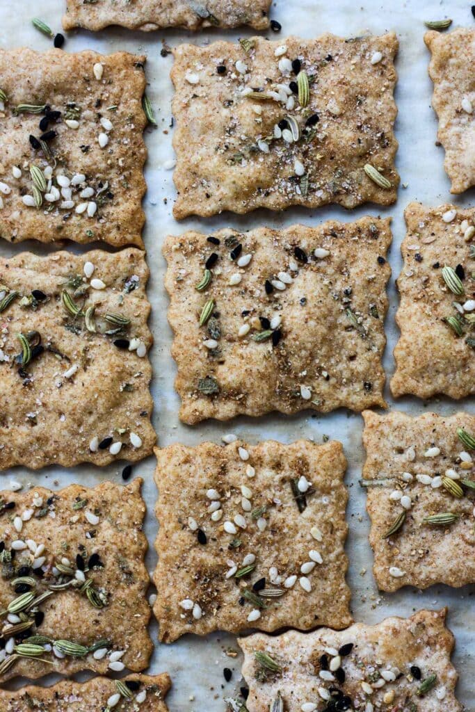 homemade sourdough crackers lying flat on baking sheet sprinkled with seeds and herbs.