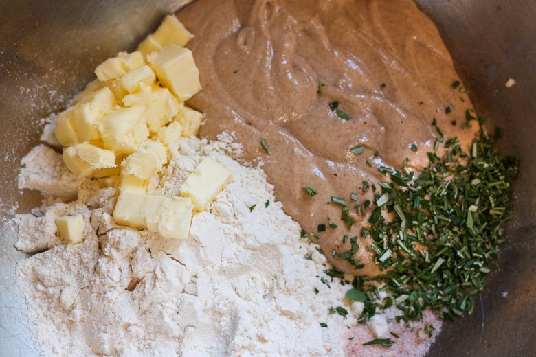 making sourdough crackers by mixing together sourdough starter, chopped herbs, butter cubes, and flour together in large bowl.