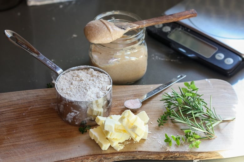 sourdough crackers ingredients- sourdough discard, flour, butter, salt, and fresh herbs on wood board.