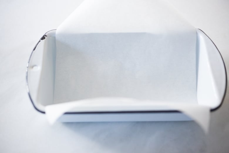 placing parchment paper in glass loaf pan.