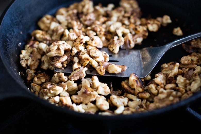 cast iron skillet with walnuts toasting with metal spatula.