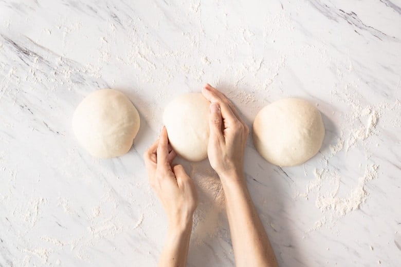 Using a circular cupping motion with the palm of your hand, gently roll each ball of dough on the countertop to create a taut ball.