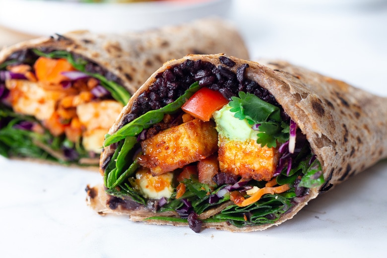 Scrumptious Thai Burrito with Peanut Sauce, baked peanut Tofu, black rice, spicy sriracha black beans and shredded crunchy veggies all wrapped up in a warm, whole wheat tortilla. #vegan #veganburrito #thaiburrito 