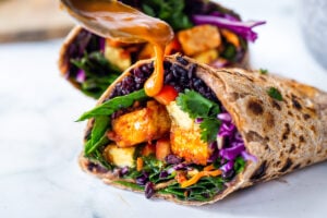 Scrumptious Thai Burrito with Peanut Sauce, baked peanut Tofu, black rice, spicy sriracha black beans and shredded crunchy veggies all wrapped up in a warm, whole wheat tortilla. #vegan #veganburrito #thaiburrito