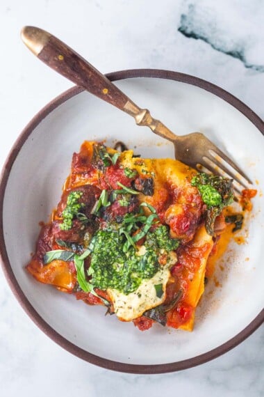 This Vegan Lasagna is made with a robust mushroom-spinach bolognese sauce, fresh basil, vegan ricotta and no-boil lasagna noodles, topped off with a creamy marinara sauce, drizzled with Arugula Basil Pesto. Vegan comfort food at its best! #veganlasagna #vegandinnerrecipes #vegan #lasagna #mushroombolognese