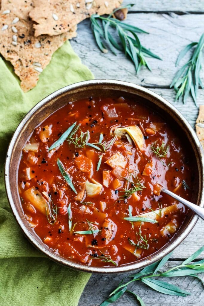 bowl of tomato artichoke soup garnished with fresh herbs with spoon in the bowl. 