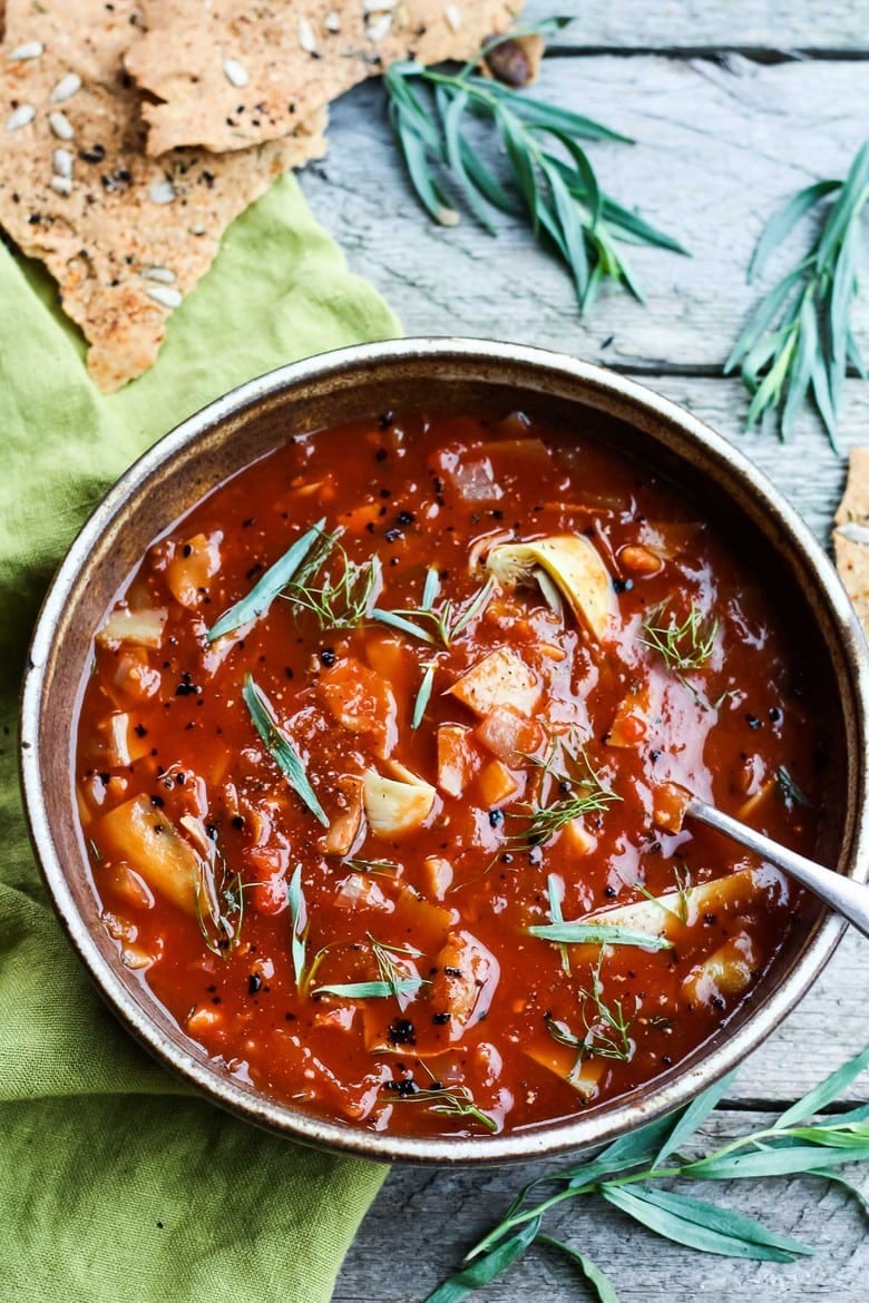 brothy tomato artichoke soup garnished with fresh herbs.