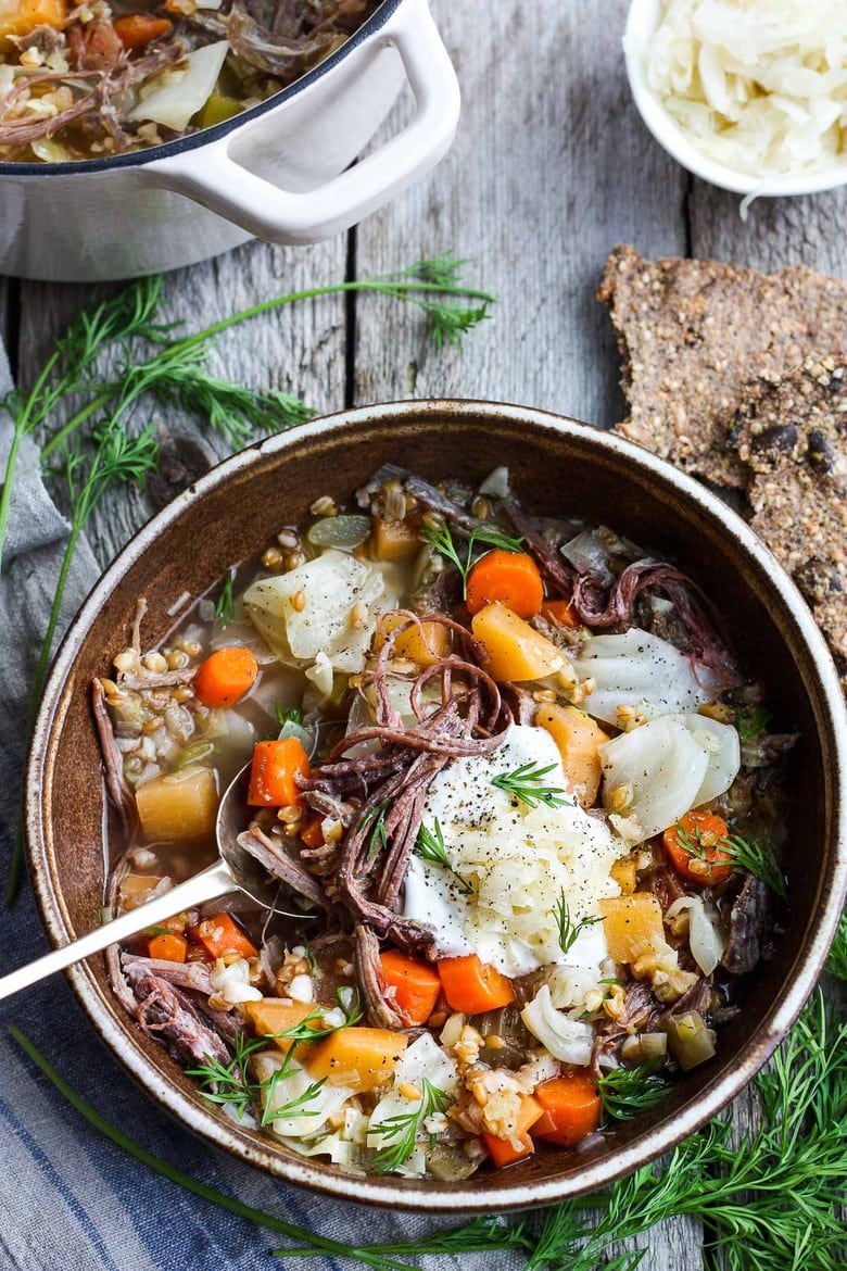 corned beef and cabbage stew in bowl with root vegetables, farro, fresh dill, sour cream, and sauerkraut.