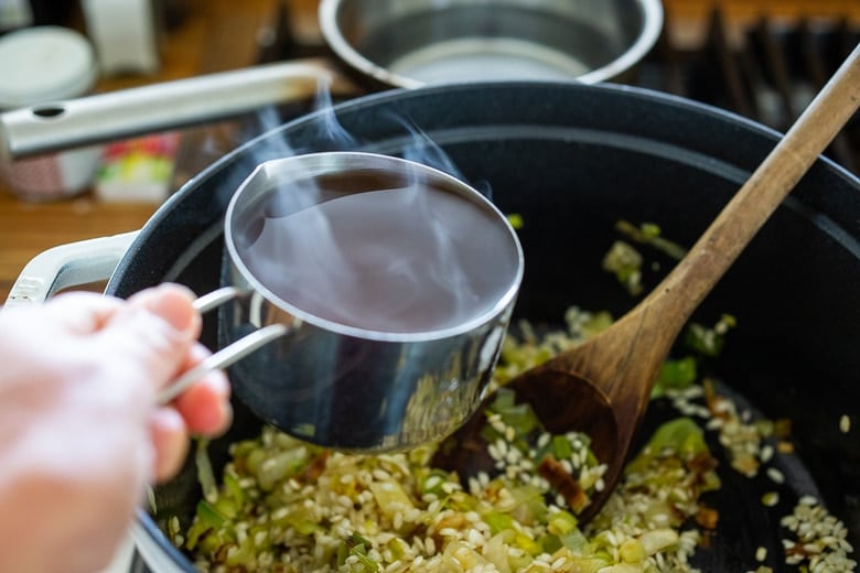 a cup of hot veggie broth added to pot of leeks and arborio rice.