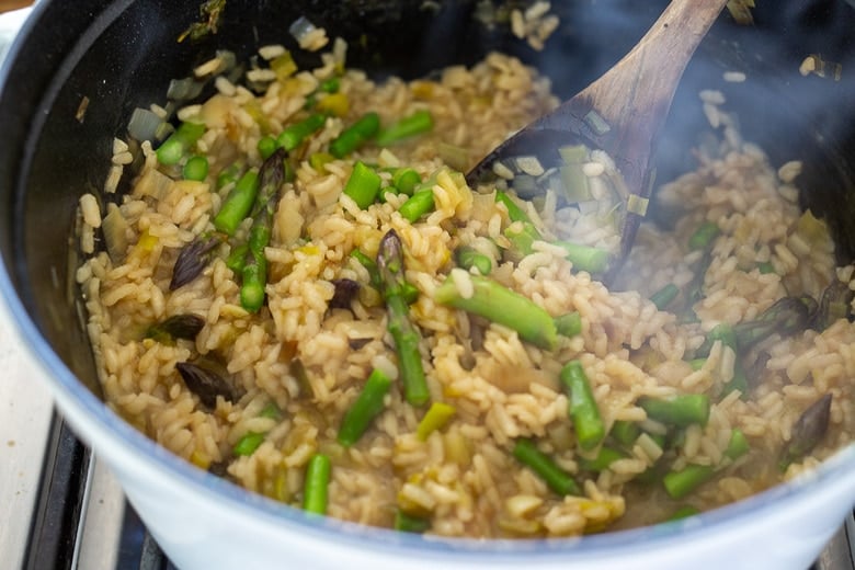 making asparagus risotto in large pot, stirring fresh asparagus into pot.