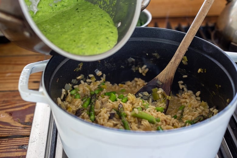 pouring in green basil asparagus sauce to pot of risotto.