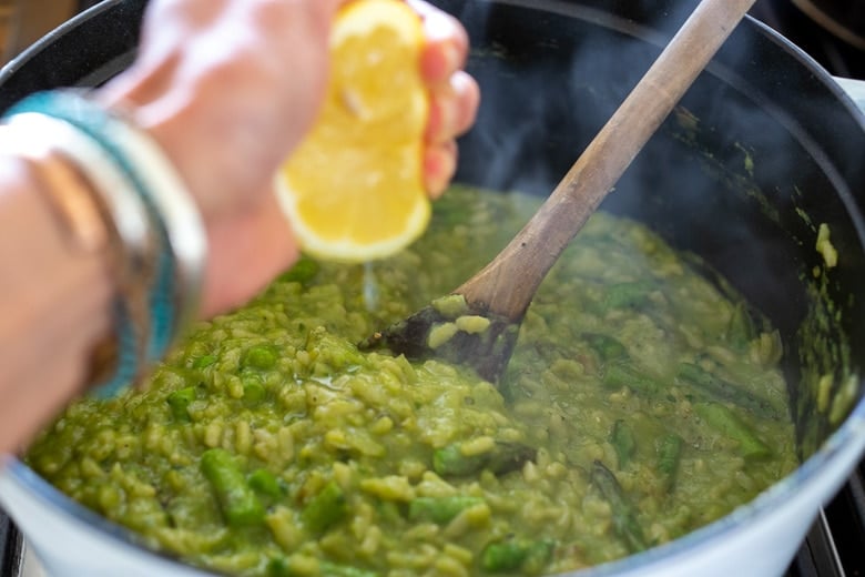 squeezing fresh lemon juice into pot of asparagus risotto.