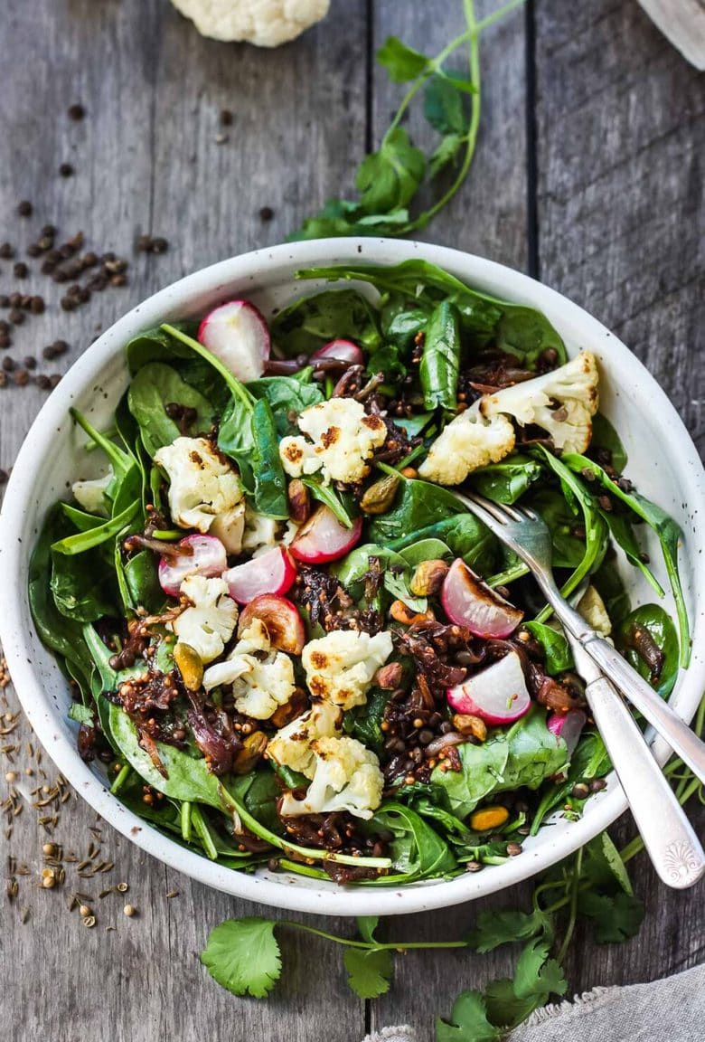 A fresh and flavorful Indian Spinach Salad with black lentils, roasted cauliflower and roasted radishes.  Caramelized shallots and a Tempered Seed Dressing give the salad amazing flavor, depth and crunchy texture. #spinachsalad #indiansalad #vegan