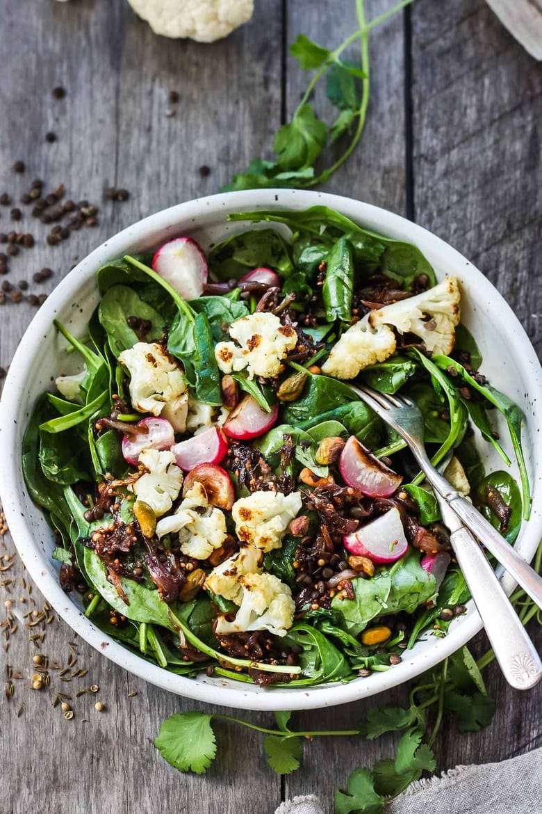 A fresh and flavorful Indian Spinach Salad with black lentils, roasted cauliflower and roasted radishes.  Caramelized shallots and a Tempered Seed Dressing give the salad amazing flavor, depth and crunchy texture. #spinachsalad #indiansalad #vegan