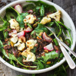 A fresh and flavorful Indian Spinach Salad with black lentils, roasted cauliflower and roasted radishes. Caramelized shallots and a Tempered Seed Dressing give the salad amazing flavor, depth and crunchy texture. #spinachsalad #indiansalad #vegan