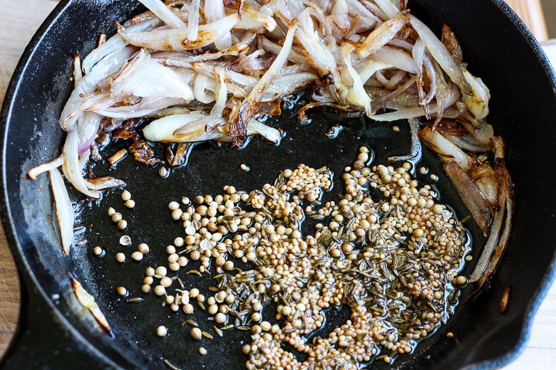 tempered seed dressing for spinach salad in a skillet with shallots