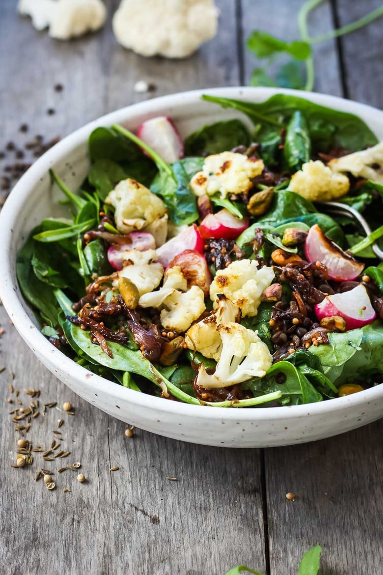 A fresh and flavorful Indian Spinach Salad with black lentils, roasted cauliflower and roasted radishes.  Caramelized shallots and a Tempered Seed Dressing give the salad amazing flavor, depth and crunchy texture. #spinachsalad #indiansalad #vegan