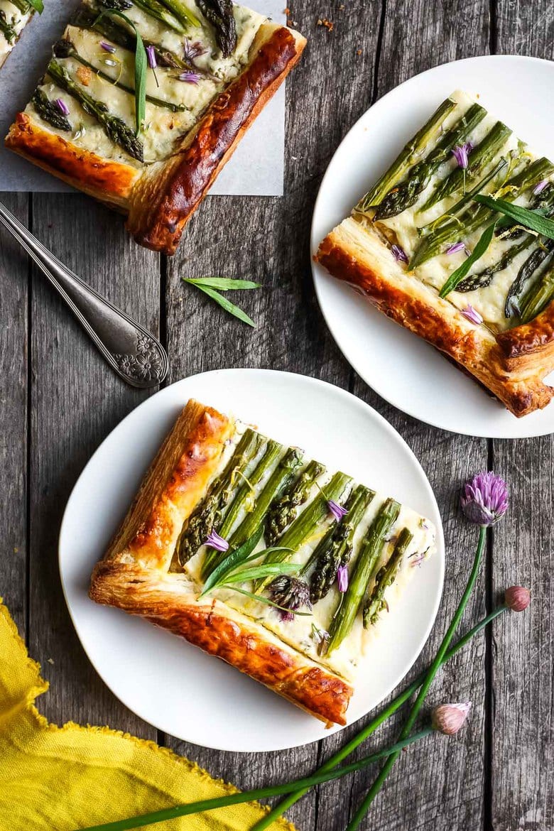 single serving squares of asparagus tart with puff pastry crust on plates, garnished with chive blossoms.