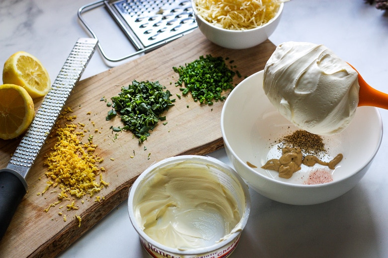 filling ingredients for the asparagus tart- bowl with salt, pepper, dijon, cream cheese, next to wood board with lemon zest, herbs, grated gruyere cheese.