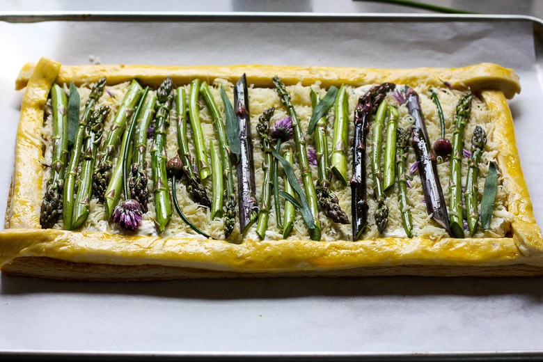 baked puff pastry with layer of grated cheese and asparagus stalks assembled on top ready to bake.