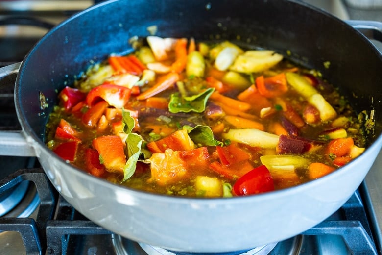 adding the veggies, broth and kaffir lime leaves to the pan, cover and simmer. 