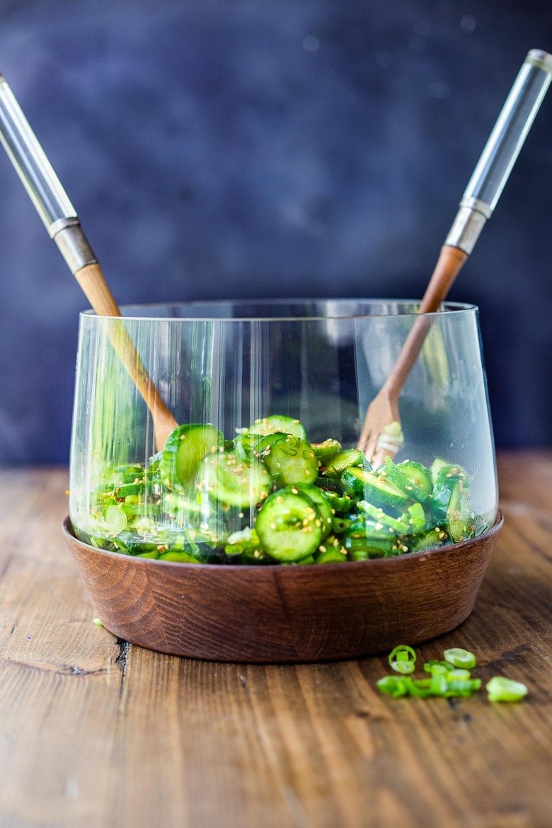 glass serving bowl with Asian cucumber salad with serving utensils.
