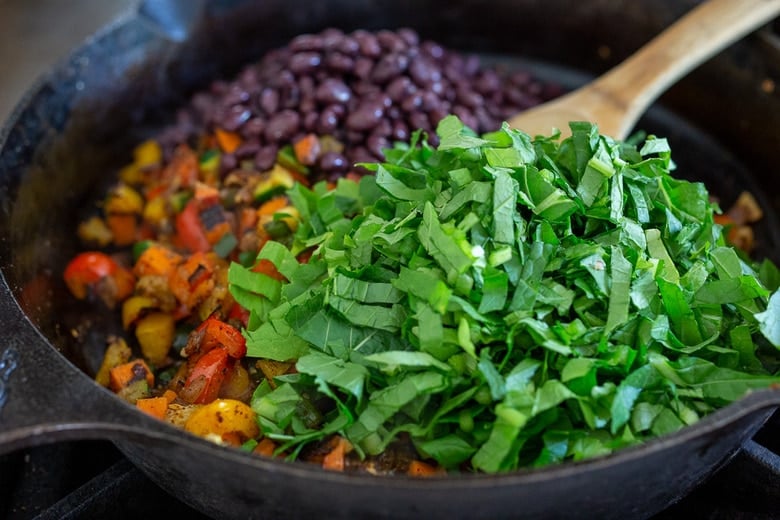 greens and blackbeans being added to the veggies in a pan